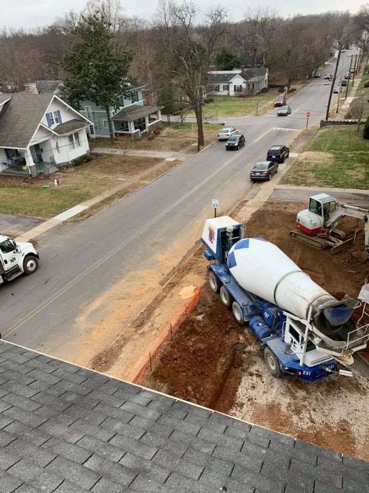 Construction site beside residential street with cement mixer truck and an excavated trench.