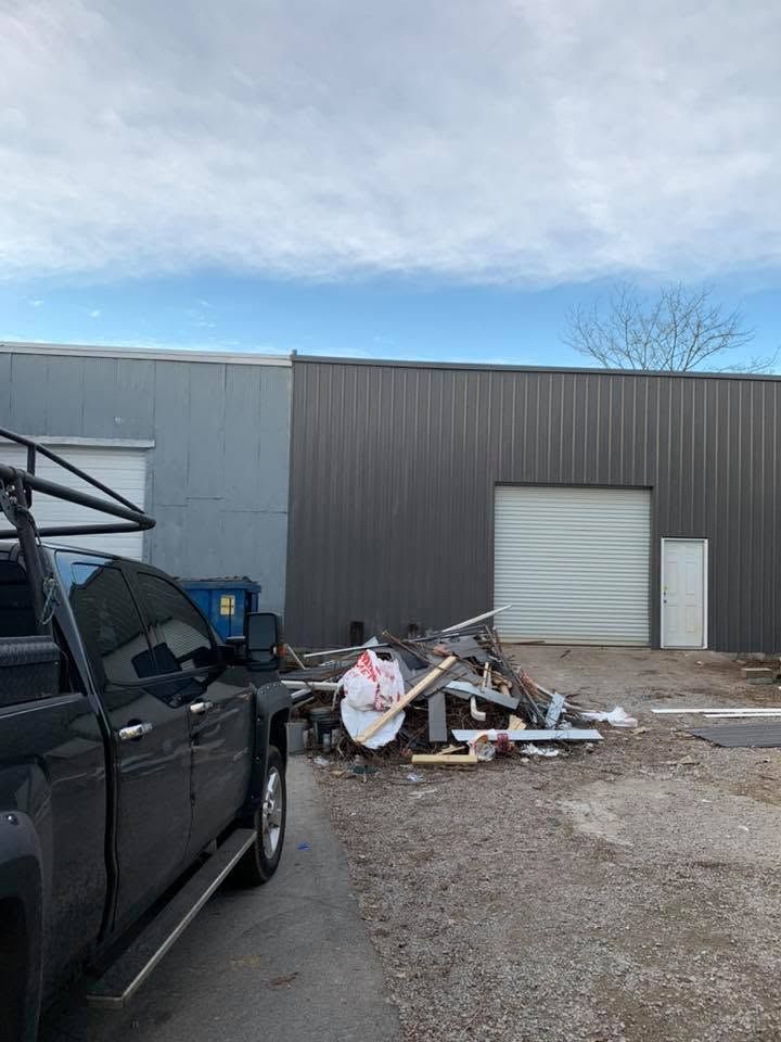 Black truck beside a warehouse loading dock with a pile of debris and trash in the lot