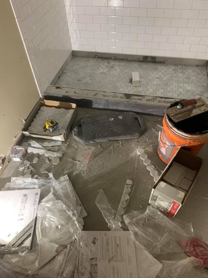 Partially tiled bathroom floor under construction, with tools, debris, and an orange bucket.