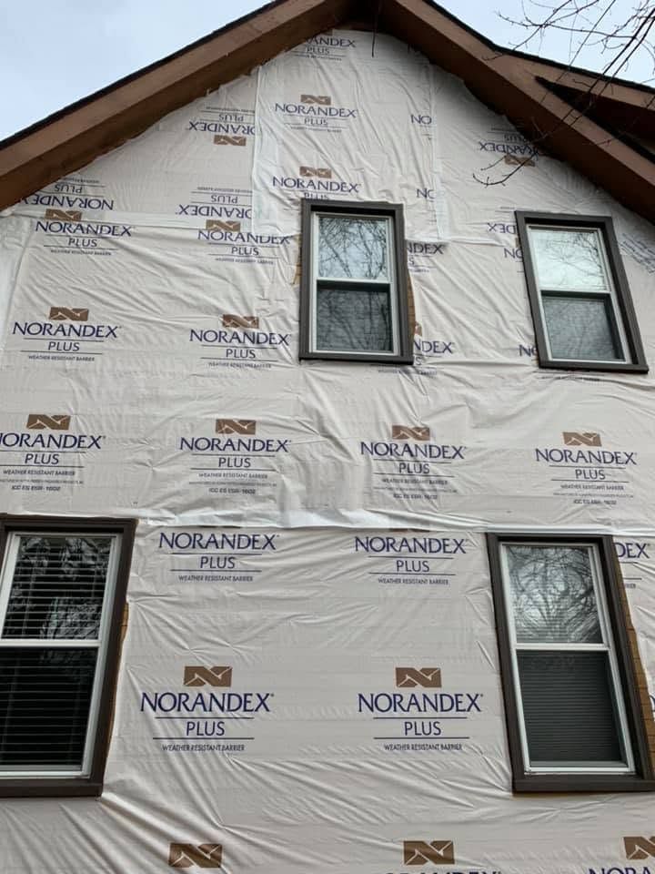House exterior under renovation with white house wrap and multiple windows under a peaked roof
