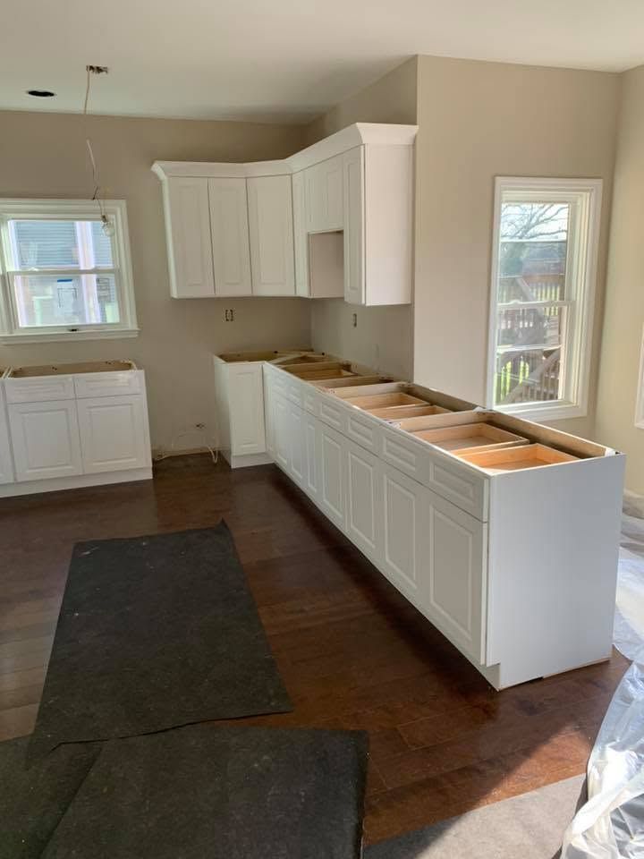 Kitchen under renovation with white cabinets, unfinished countertops, and dark wood floors