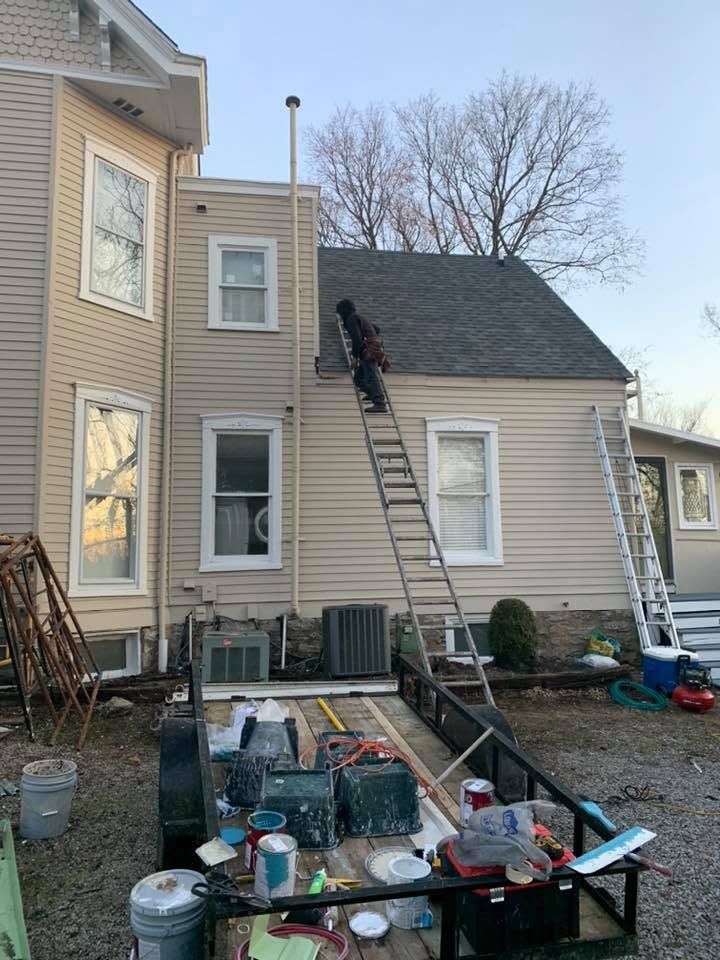 Worker on roof beside ladders at a beige house during exterior maintenance