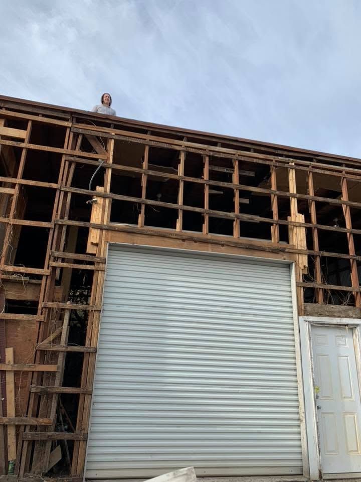 Partially demolished wooden building with exposed framing and a white roll-up garage door under a blue sky