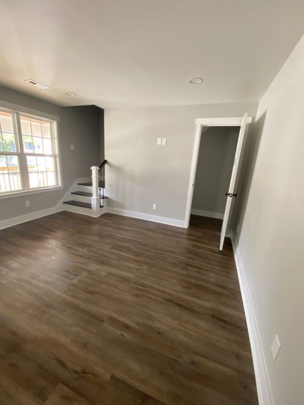 Empty room with gray walls, wood flooring, large window, and white staircase railing.