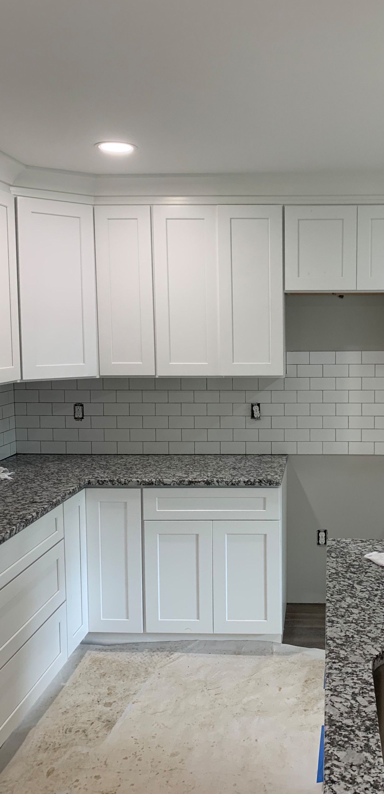 Small kitchen with white cabinets, gray countertops, and light tile backsplash under a ceiling light.