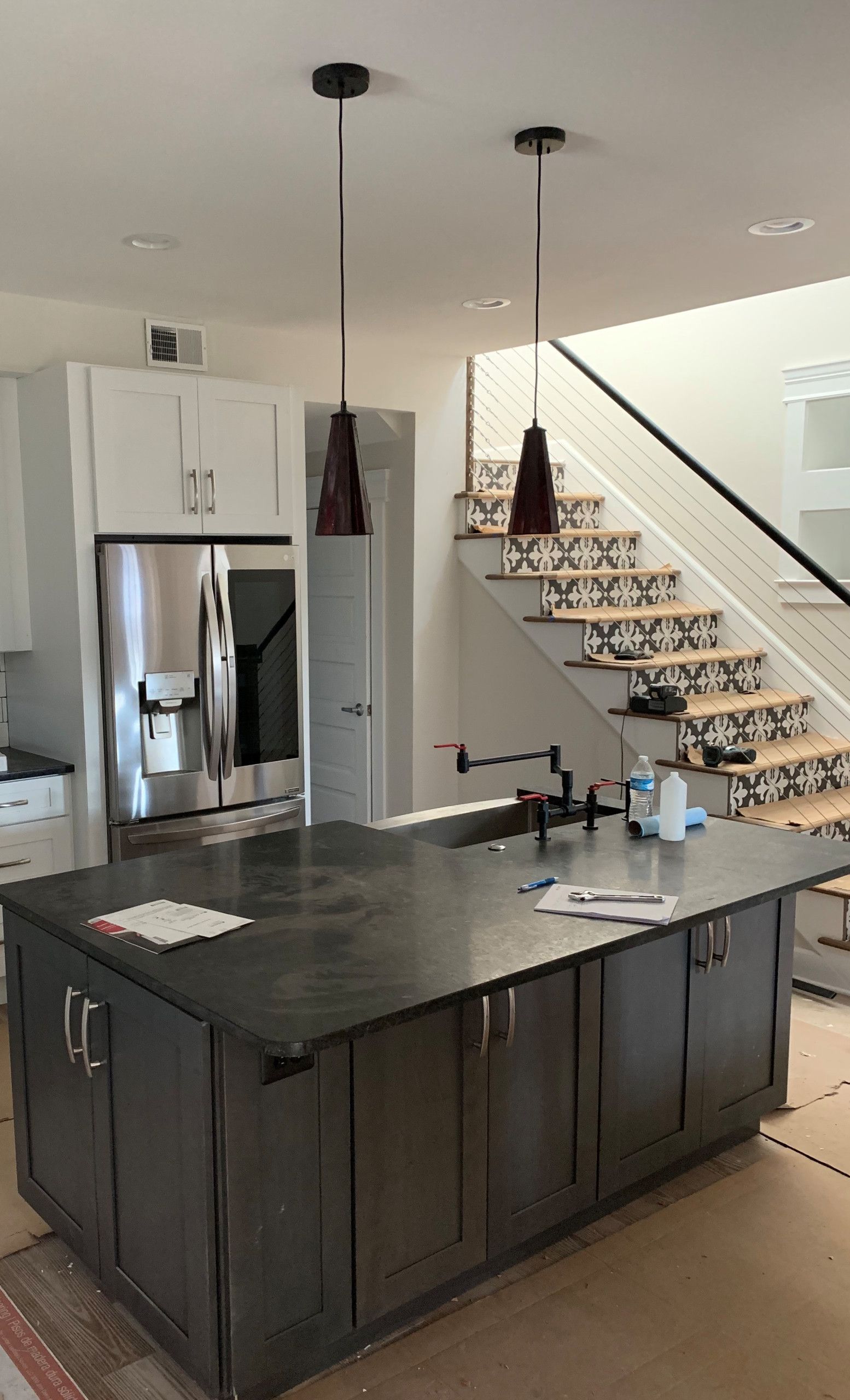 Modern kitchen with dark island, stainless refrigerator, and staircase with decorative steps.