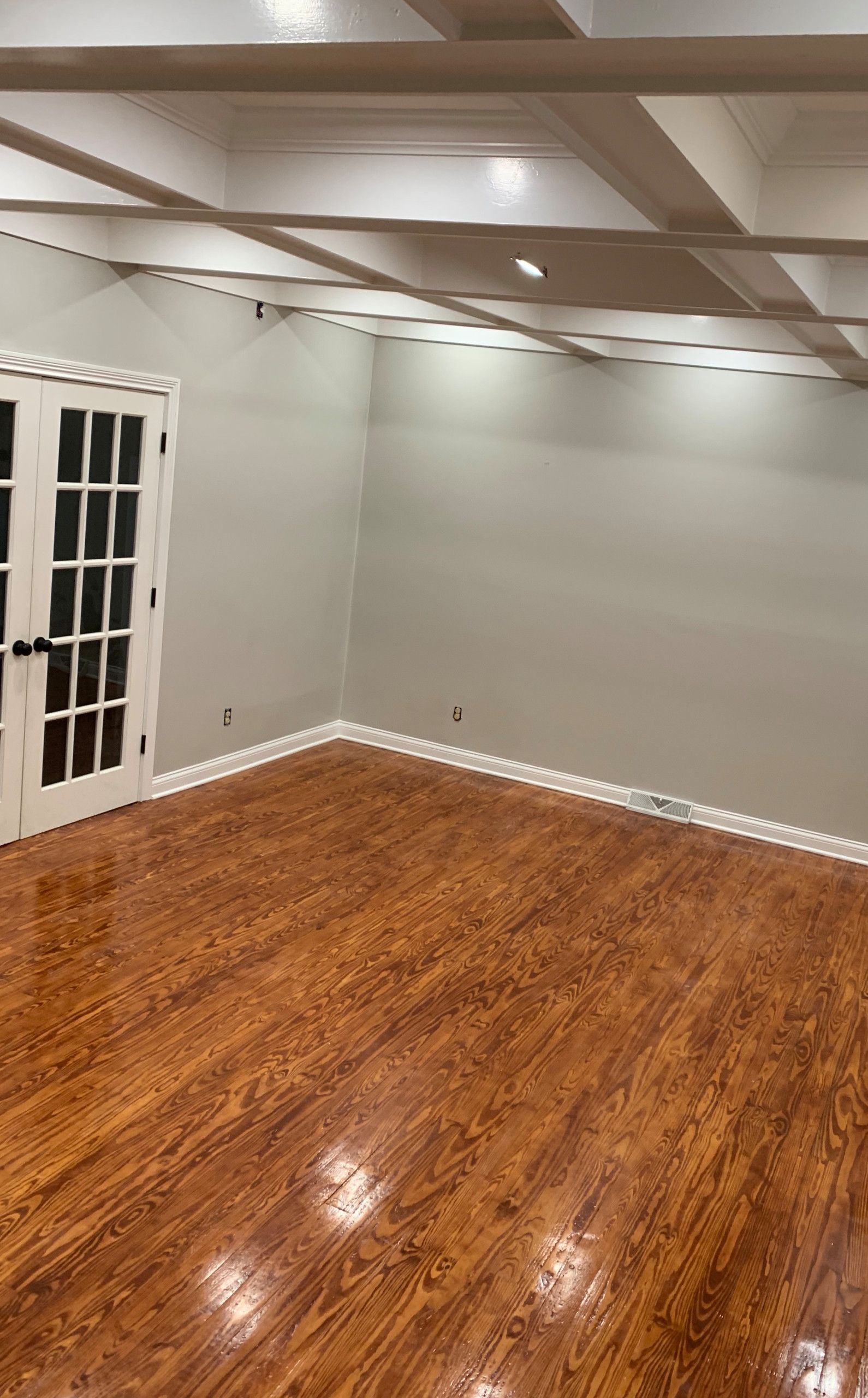 Empty room with wood floor, gray walls, white ceiling beams, and French doors on the left.