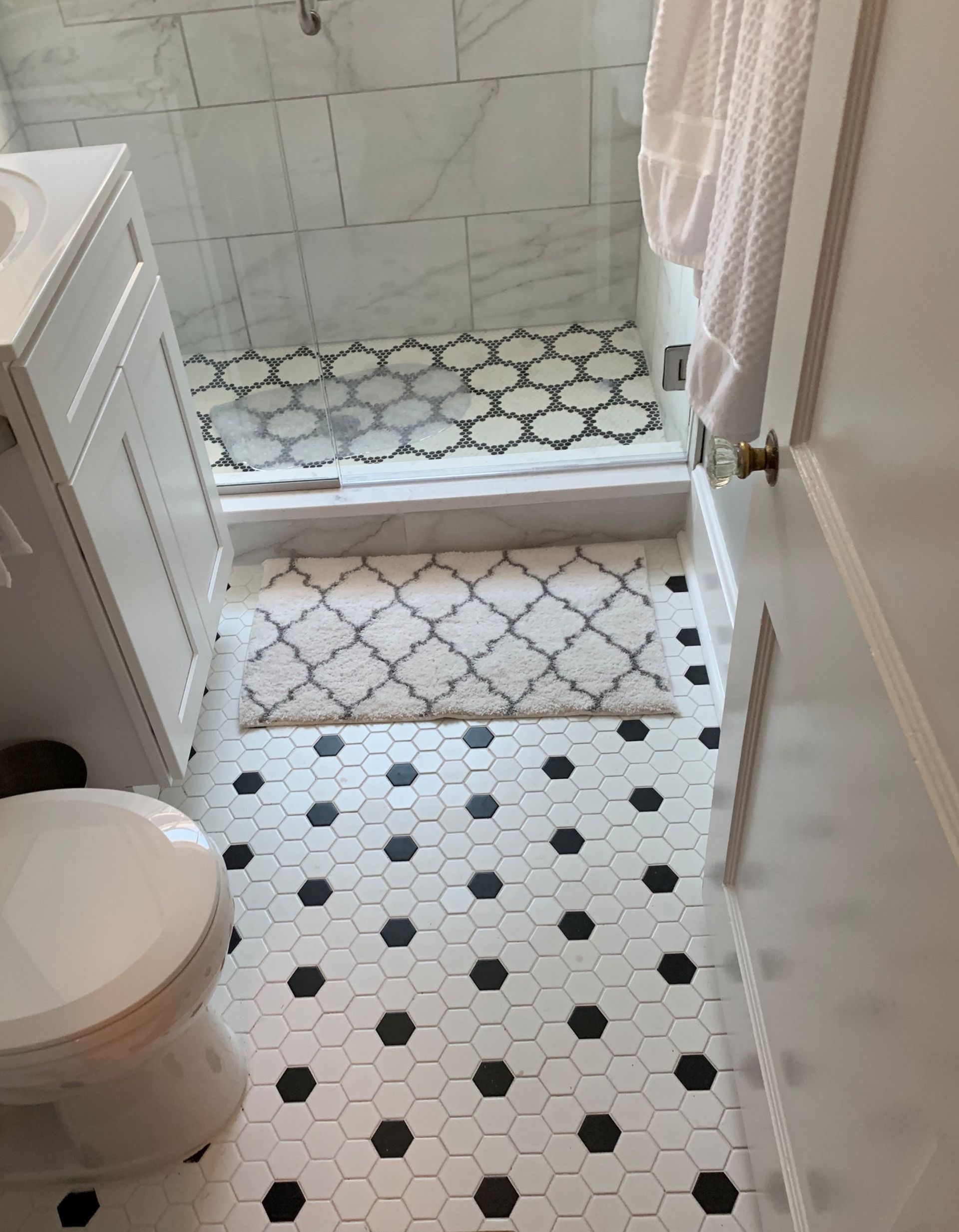 Small bathroom with white-and-black tile floor, step-up shower, toilet, and shower curtain