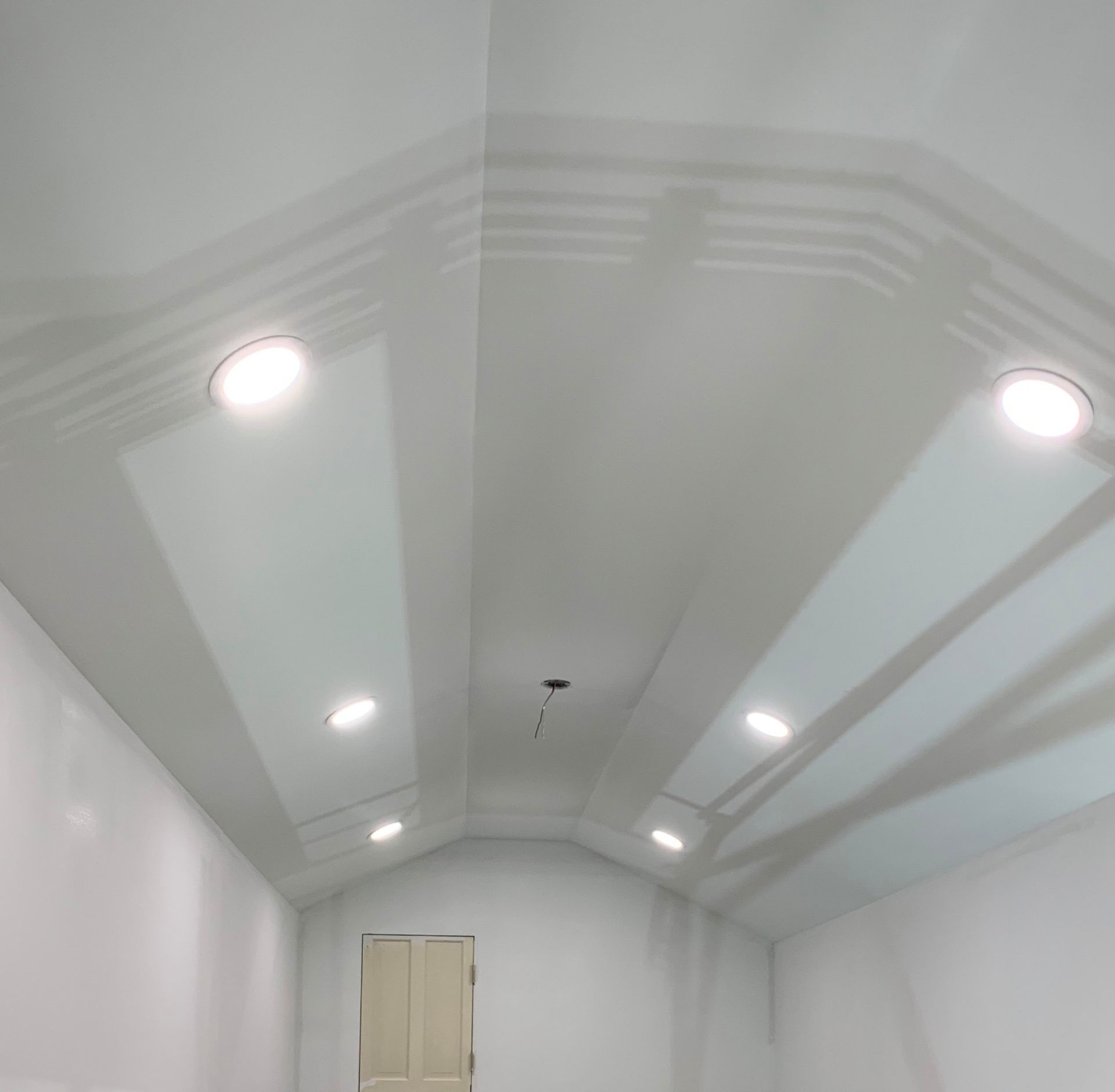 Bright white vaulted room with recessed ceiling lights and double doors at the far end