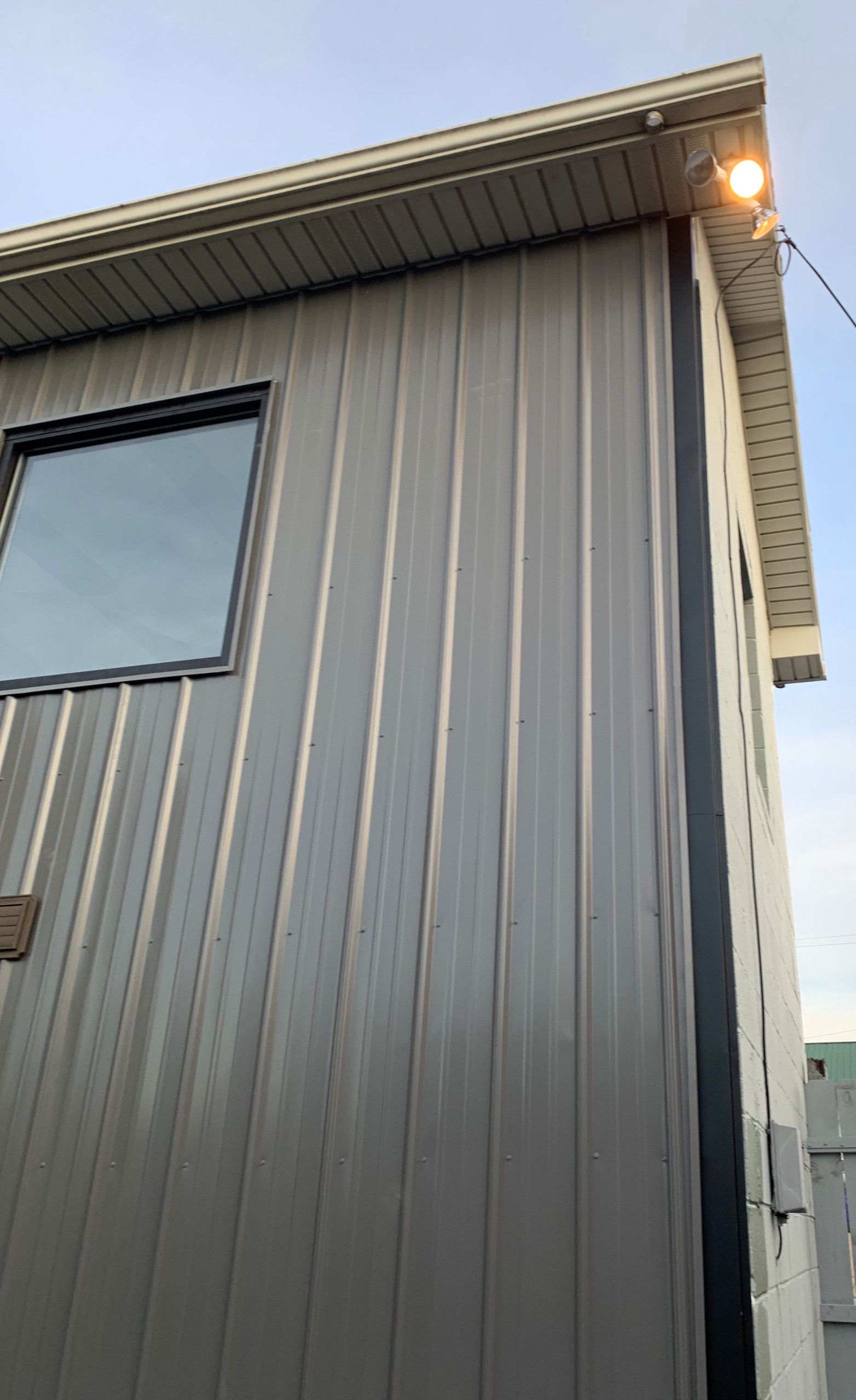 Gray metal-sided building exterior with a window and lit light under the roof eave