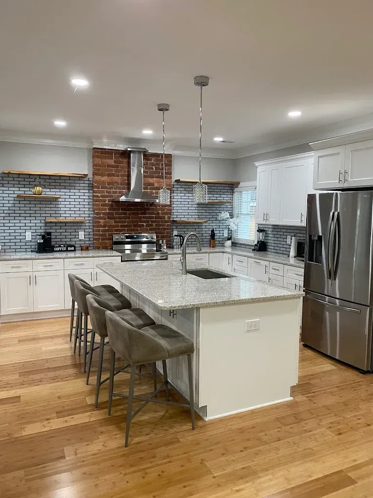 Bright modern kitchen with white cabinets, granite island, stainless steel fridge, and brick backsplash.