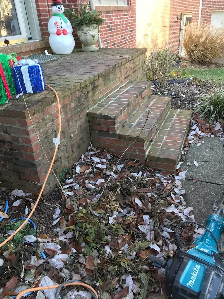 Brick front steps with a snowman decoration, gift boxes, and fallen leaves beside a sidewalk
