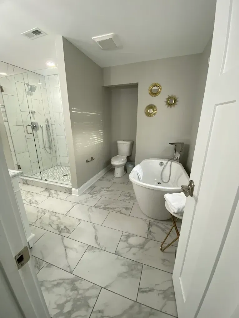 Modern white bathroom with glass shower, toilet, and freestanding tub on marble tile floor