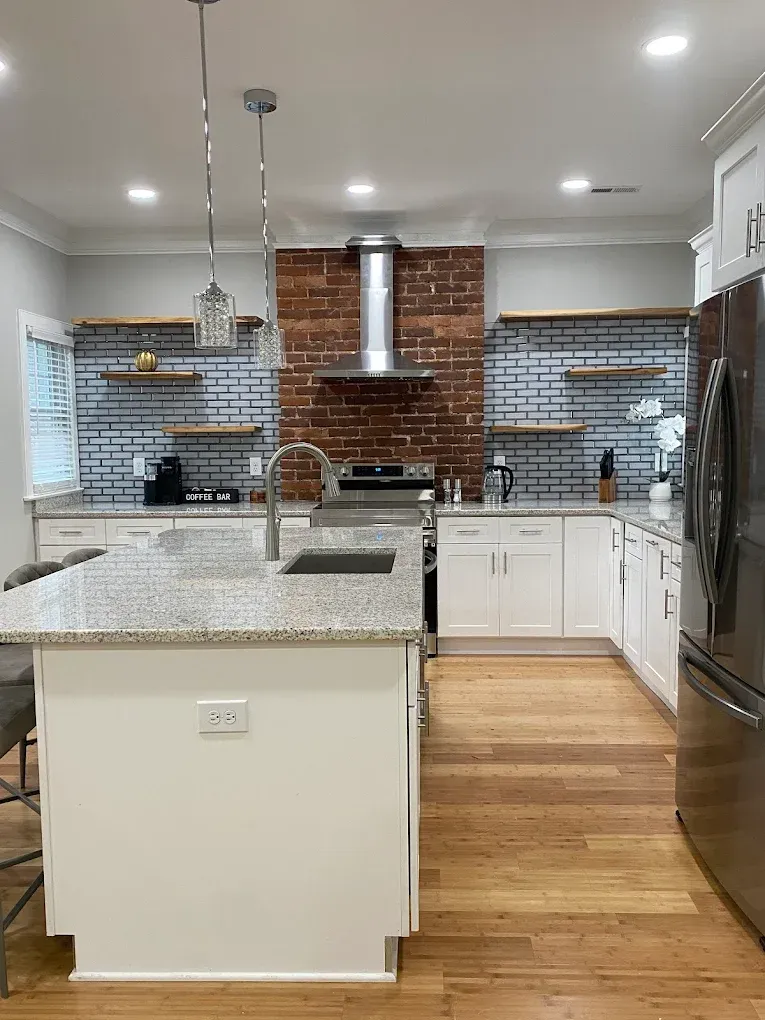 Modern kitchen with granite island, white cabinets, exposed brick backsplash, and hardwood floors