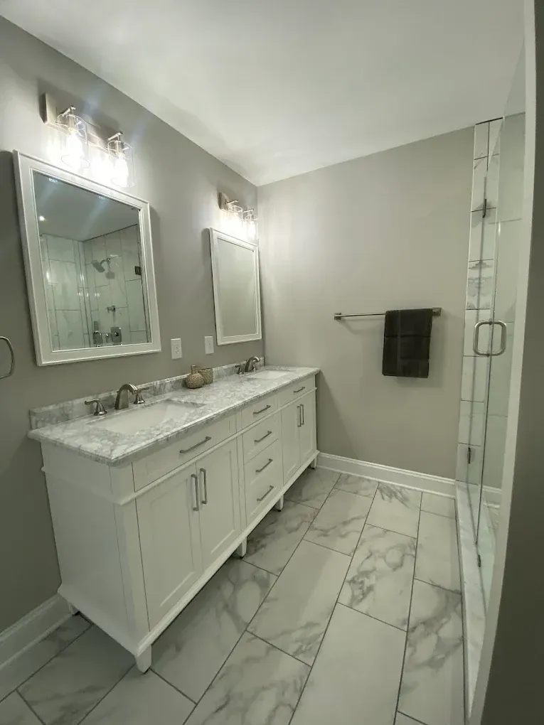 Bright modern bathroom with double vanity, marble countertop, mirrors, and glass shower door