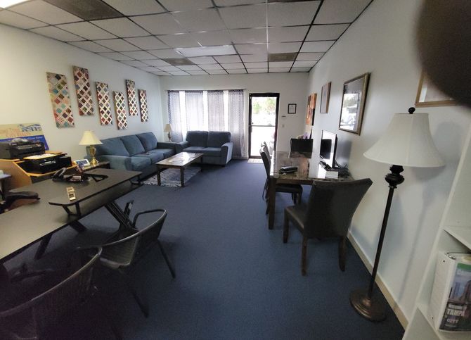 Interior office with couches, desks, and a doorway. Blue carpet and various decor.