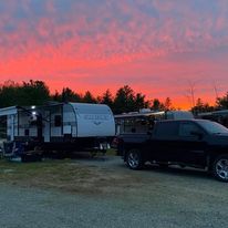 RV and black pickup truck at a campsite under a pink sunset sky