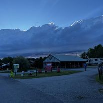 Dusk over a rural building and gravel road, with dark clouds and mountains in the background.
