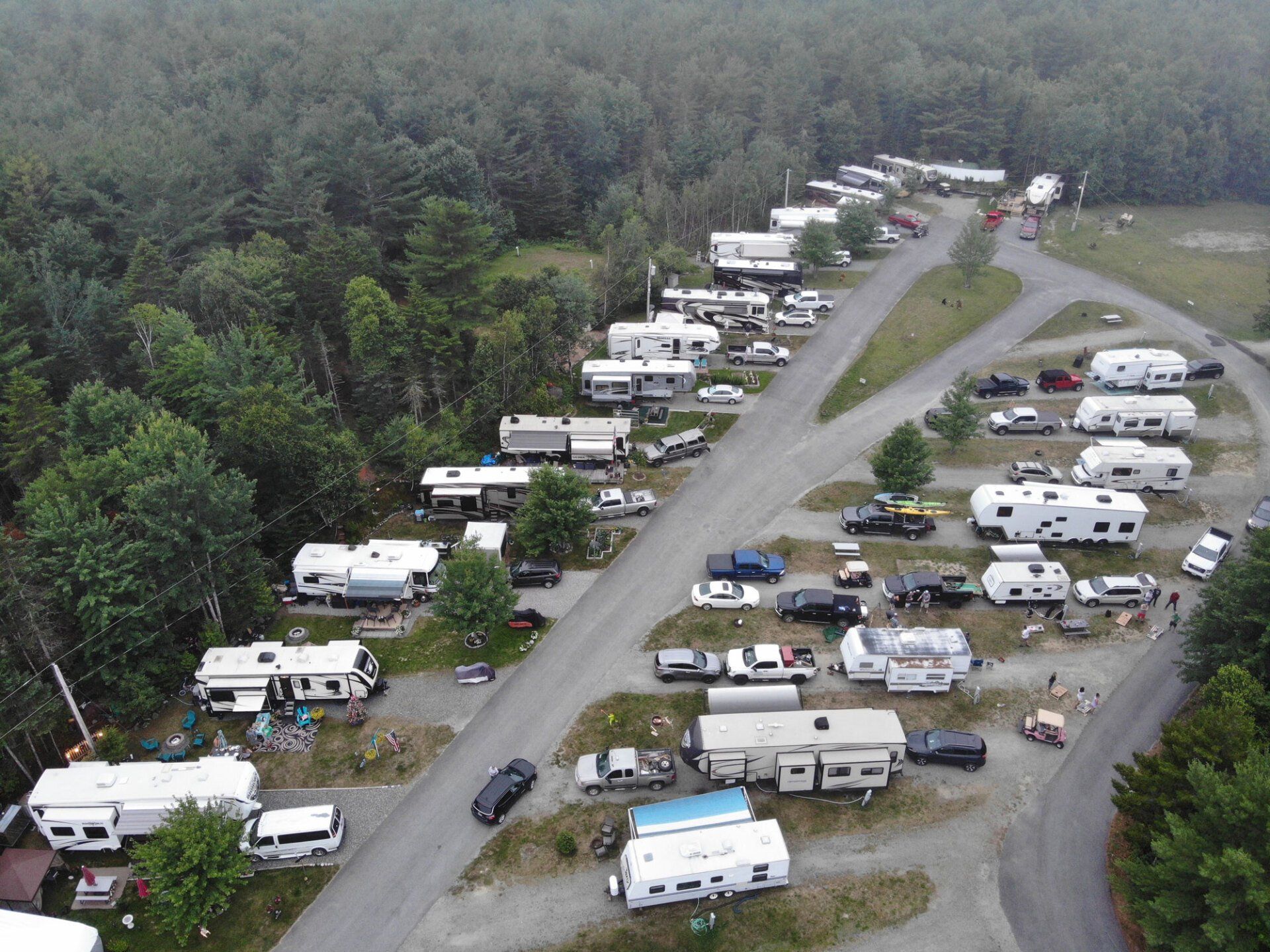 Aerial view of an RV campground with rows of campers along gravel roads beside a forest.