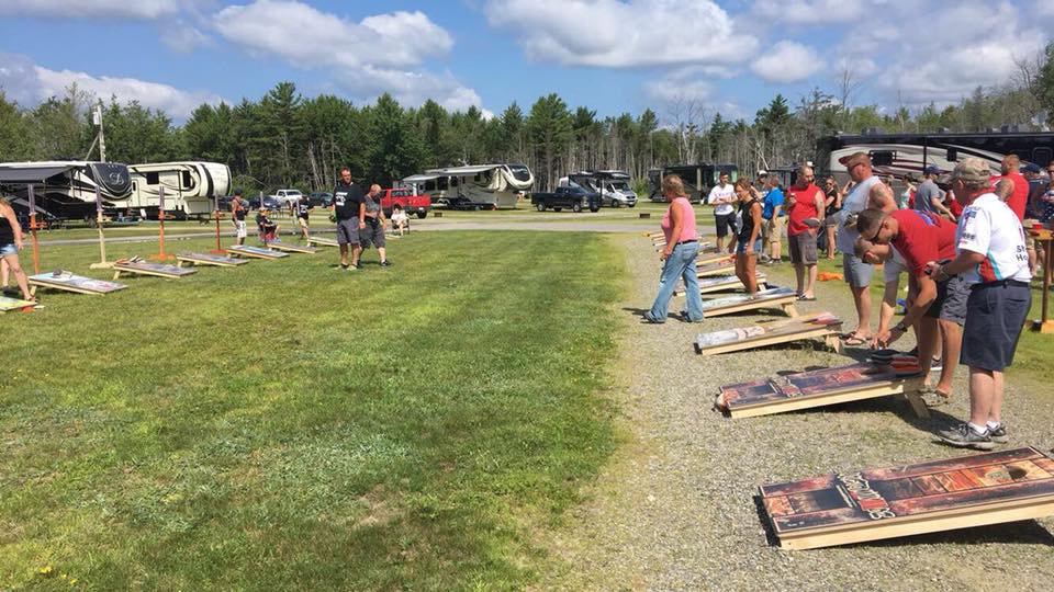 People lined up outdoors at a cornhole toss event on a sunny grassy field.