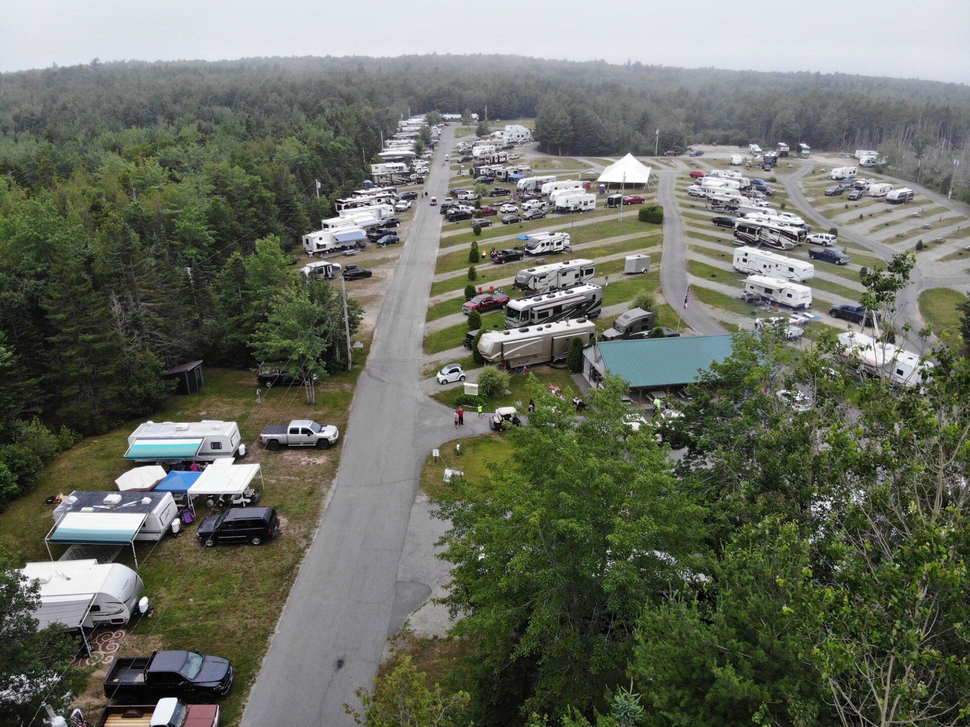 Aerial view of a wooded RV campground with parked campers, tents, and a central road