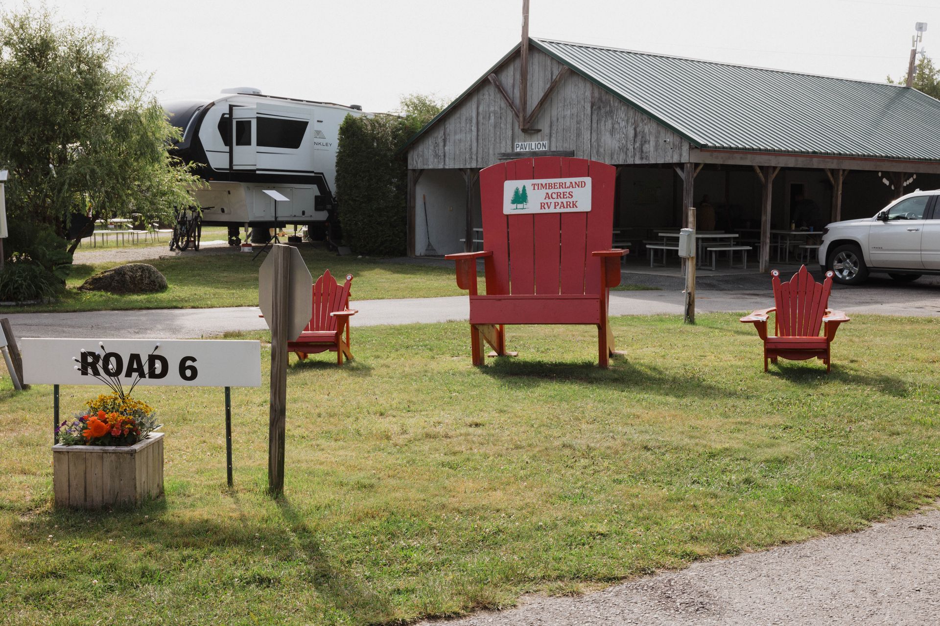 Road 6 sign beside red chairs, grassy yard, and a building with an RV in the background