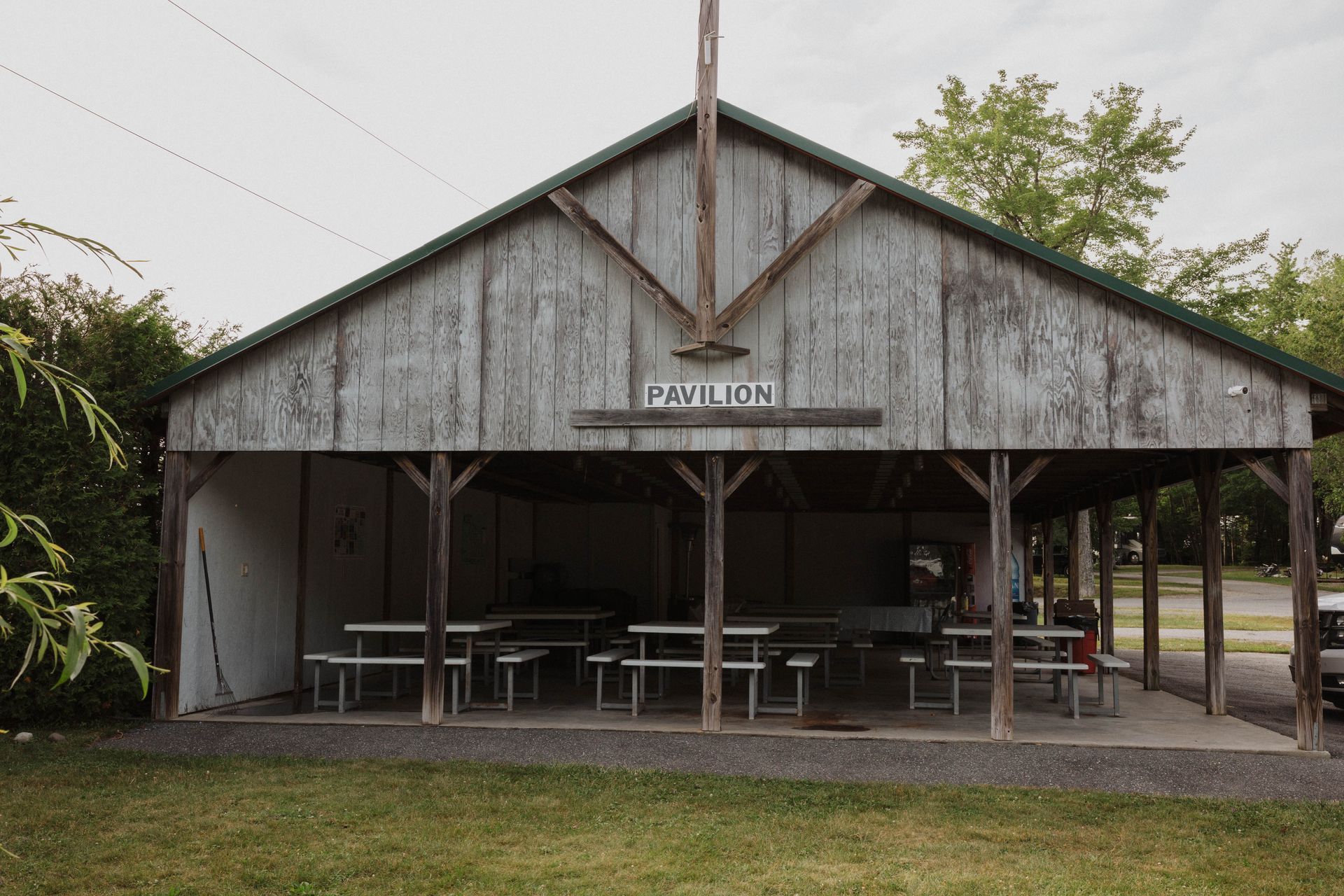 Rustic open-air pavilion with weathered wood siding, picnic tables, and a grassy foreground