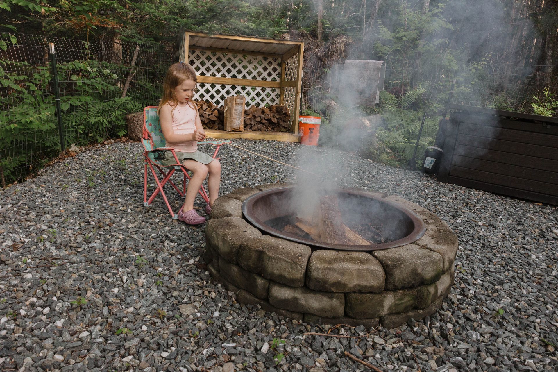 Child sitting by a smoky backyard fire pit on a gravel patio