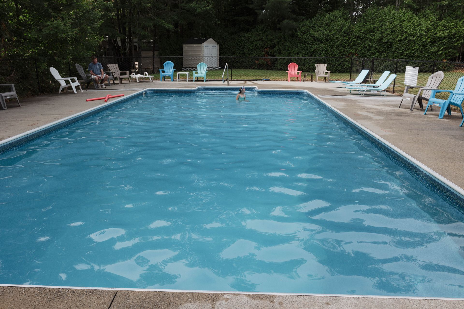 Outdoor swimming pool with blue water, lounge chairs, and trees around the deck
