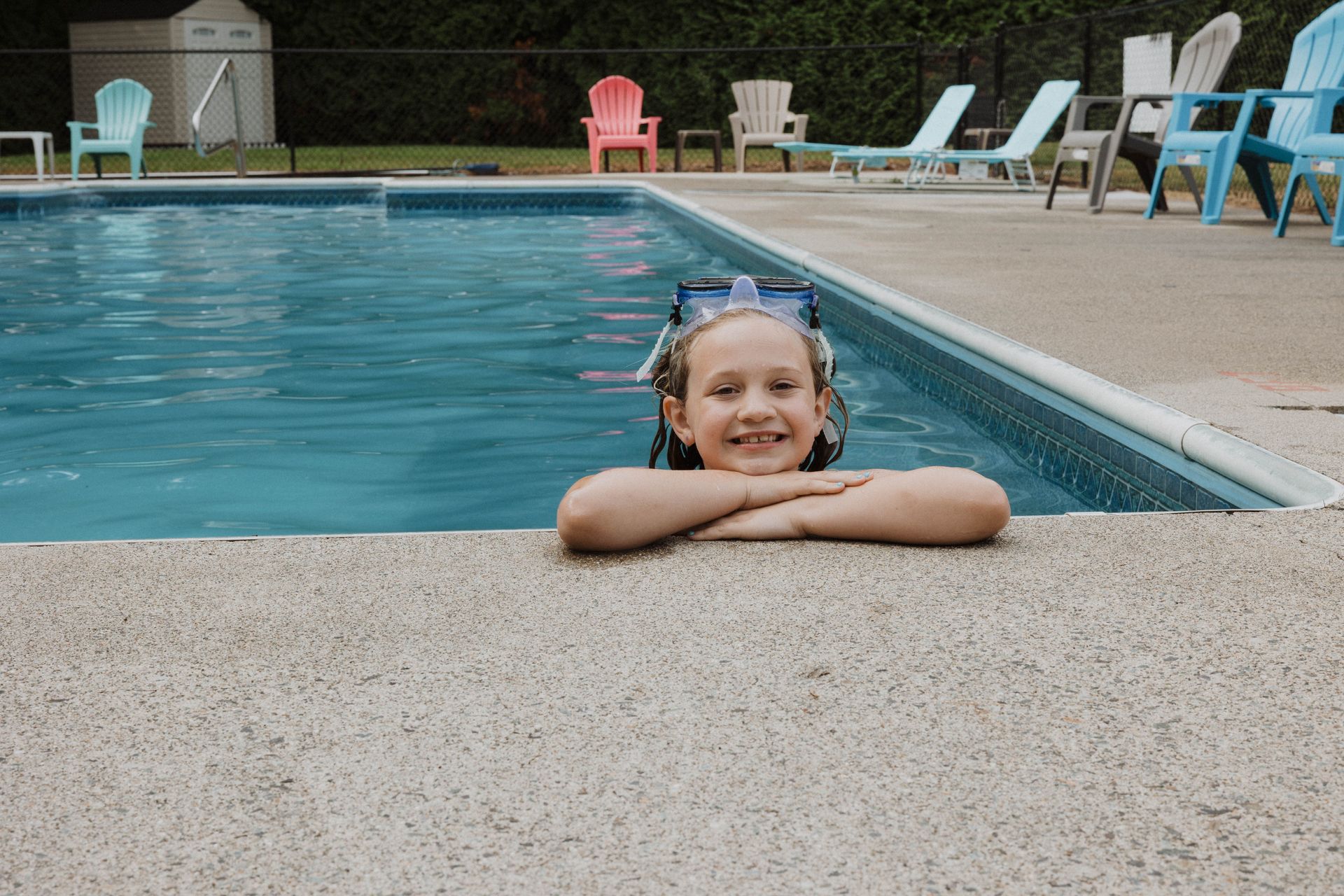 Child smiling with arms on pool edge beside a blue swimming pool