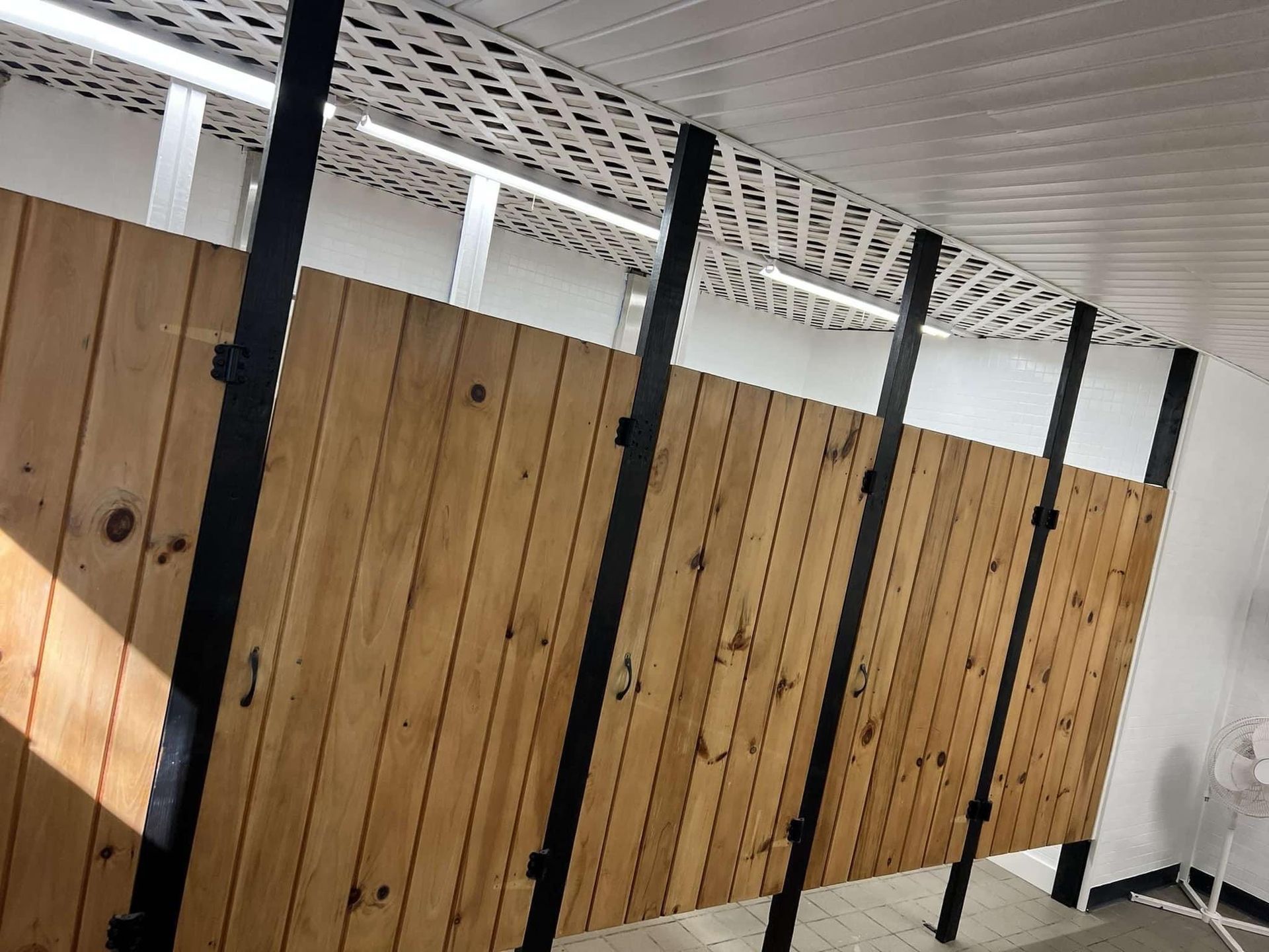 Row of wooden restroom stall doors with black metal dividers under a white ceiling
