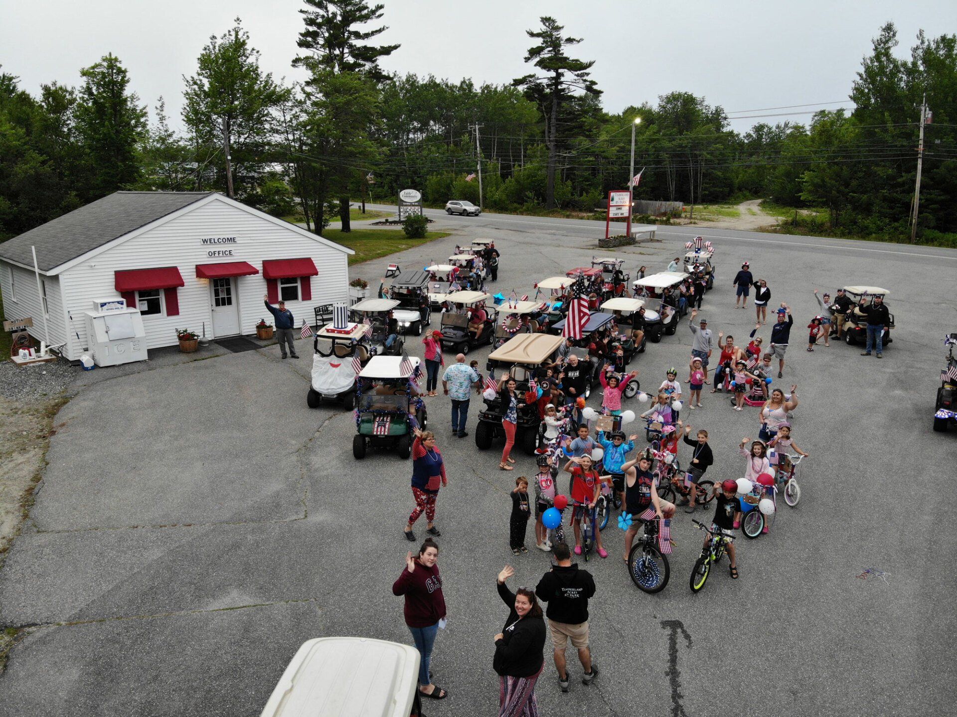 Crowd gathered with bikes and golf carts outside a white building in a gravel lot
