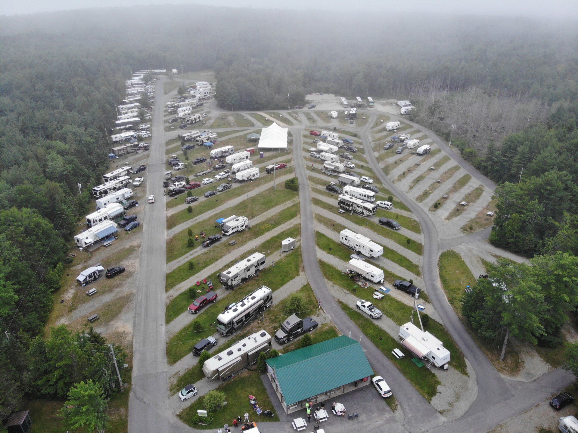 Aerial view of a crowded RV and camper campground with tents and tree-lined roads in a misty forest