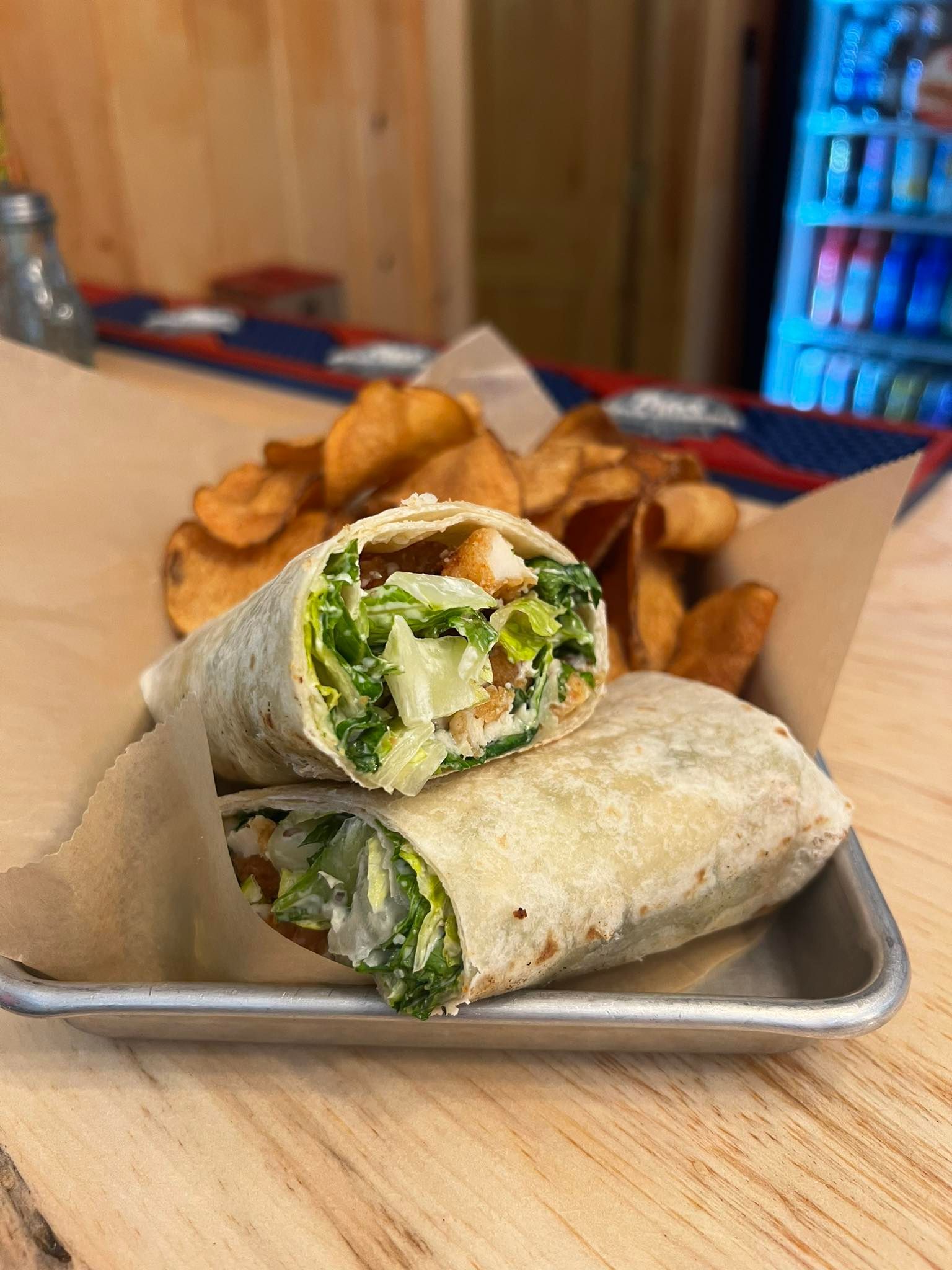 Wrap sandwich with greens and potato wedges on a tray at a table