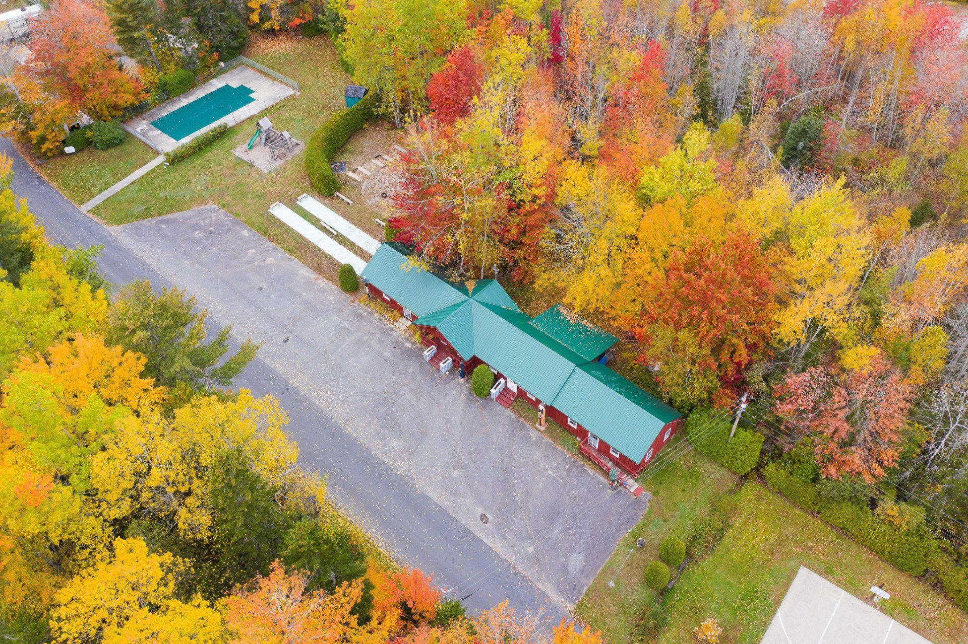 Aerial view of a parking lot beside colorful autumn trees and a green-roofed building with a pool.