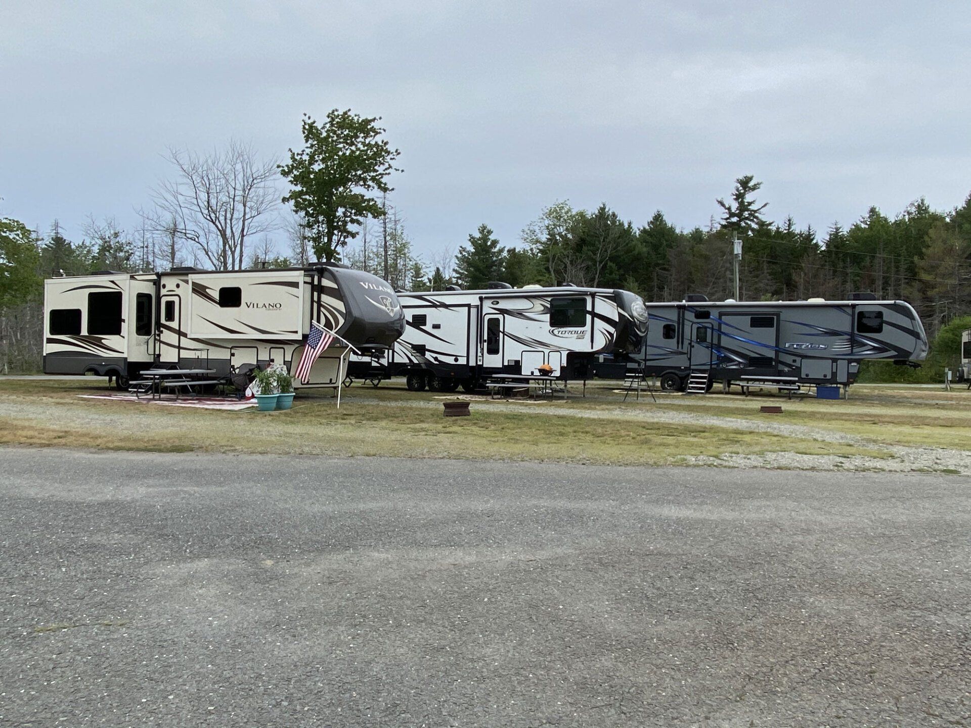 Several RV trailers parked in a row on a grassy lot under an overcast sky.