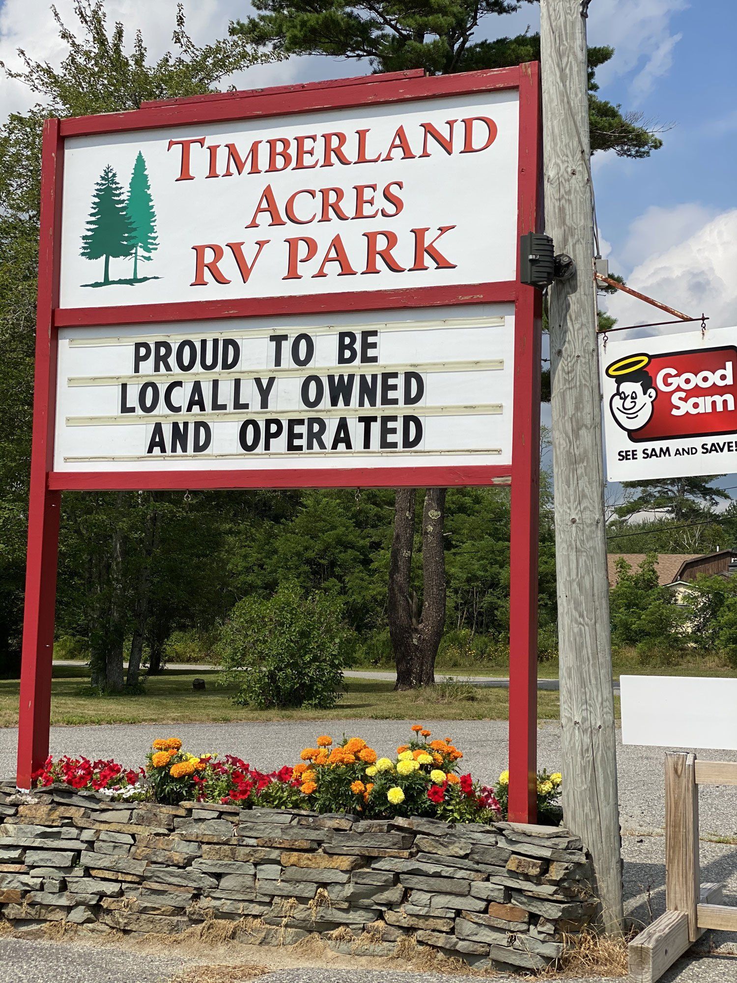 Timberland Acres RV Park sign with flowers and a Good Sam logo in front of trees