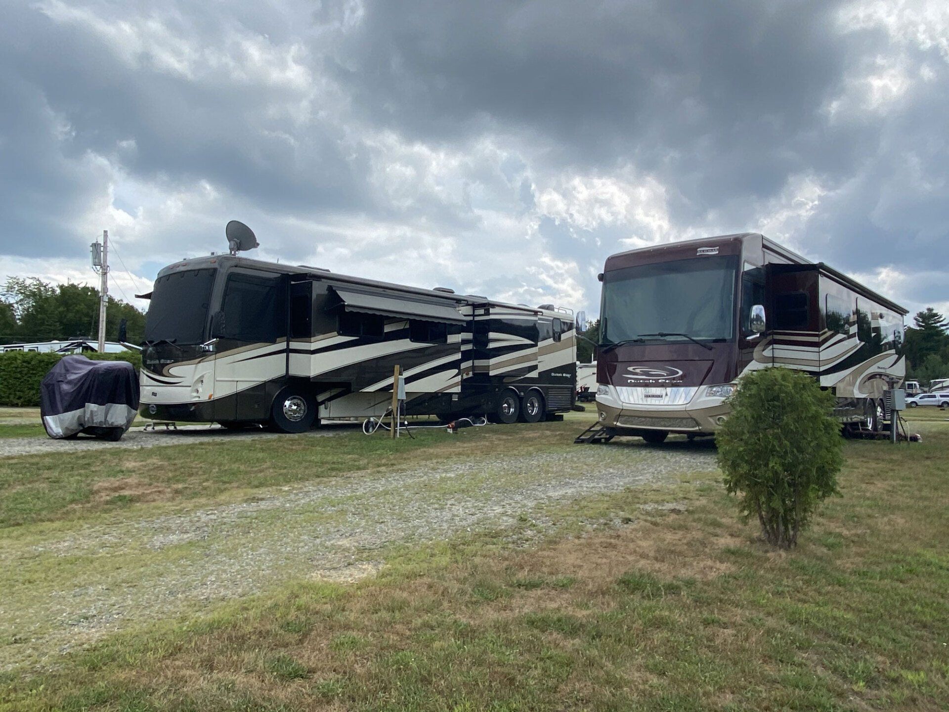 Two RVs parked on a grassy lot under cloudy skies.