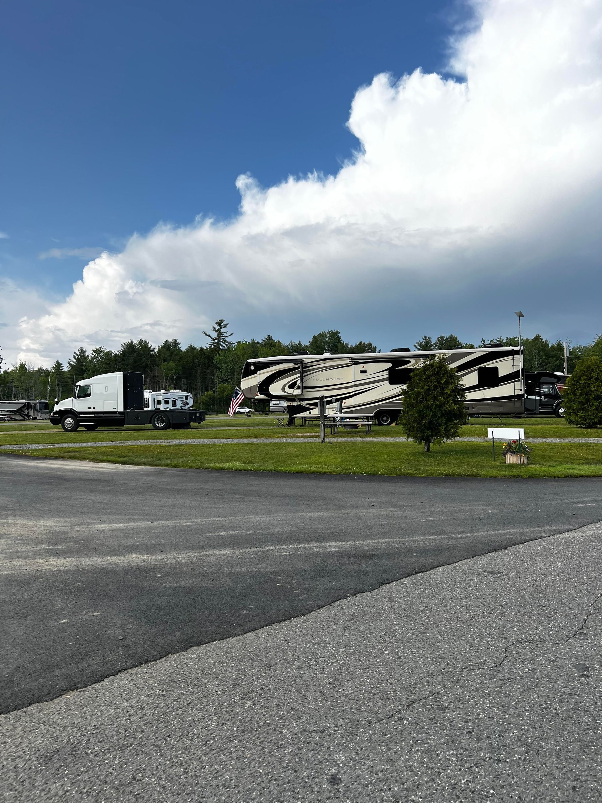 Large black-and-white RV parked in a grassy lot under cloudy sky, with a white truck nearby.