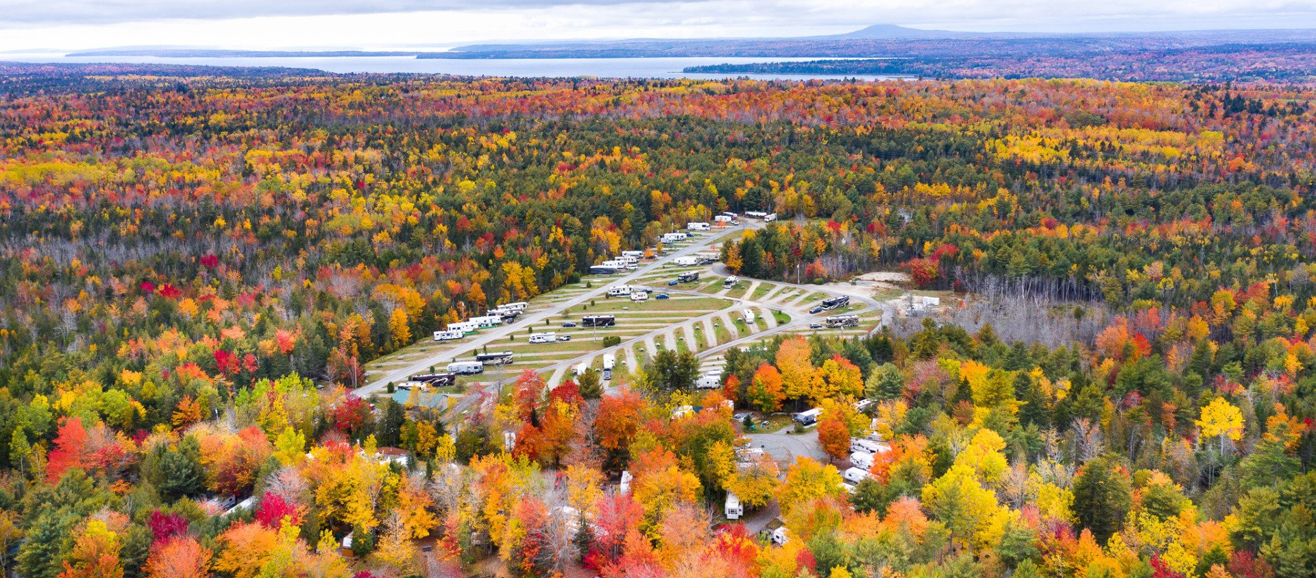 Aerial view of a winding road through a colorful autumn forest with a large parking area near the center