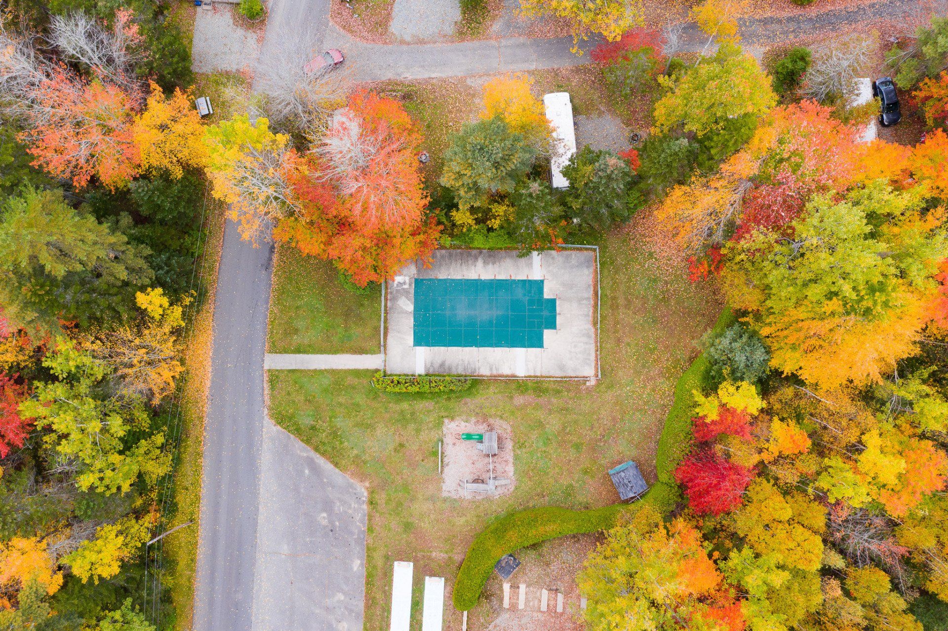 Aerial view of a house with a turquoise pool, driveway, and autumn trees surrounding the property.