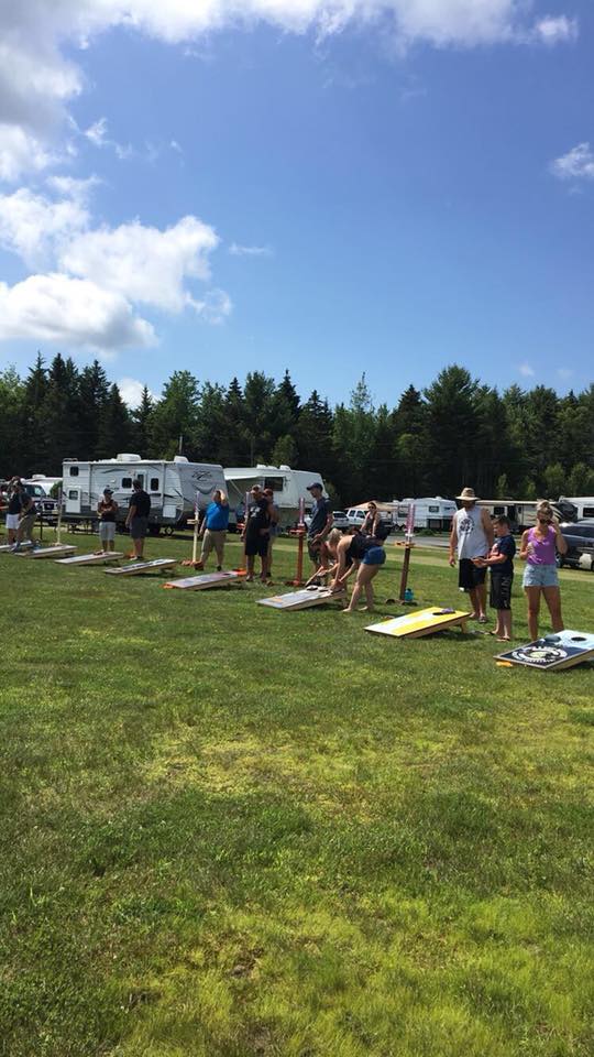 People playing lawn games on a grassy field near RVs and trees under a blue sky