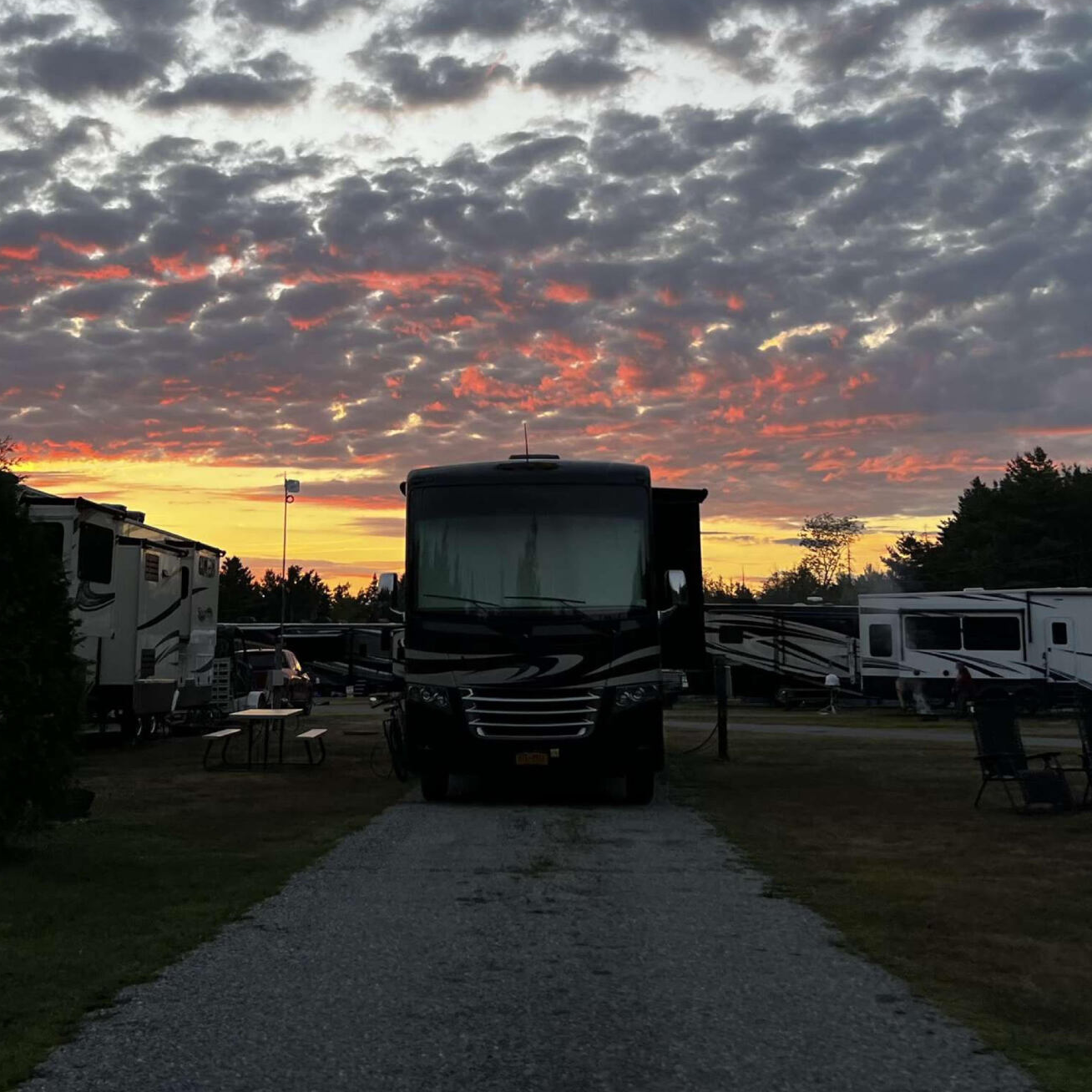 RV parked on a gravel path at dusk, with a dramatic pink-and-gray sunset sky overhead.