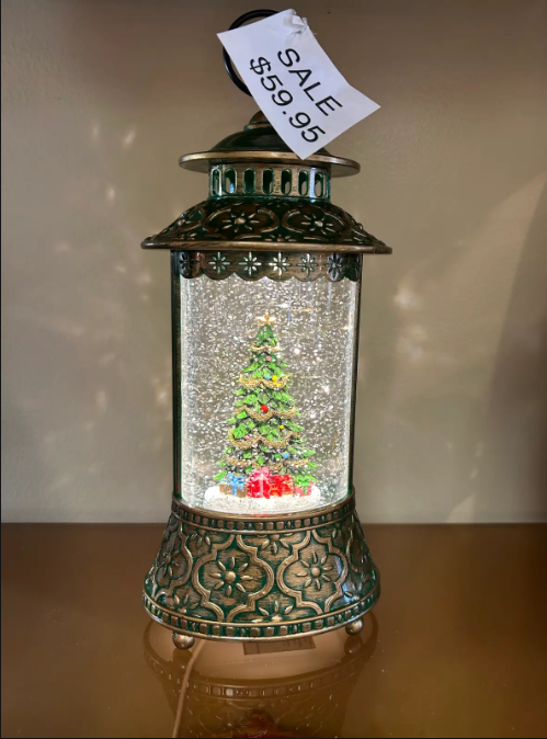 Christmas lantern with tree inside, sale tag $59.95, green and gold details, on a shelf.