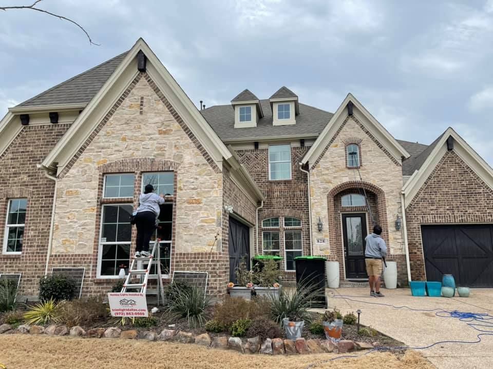 Two people cleaning windows of a two-story brick home on a cloudy day.