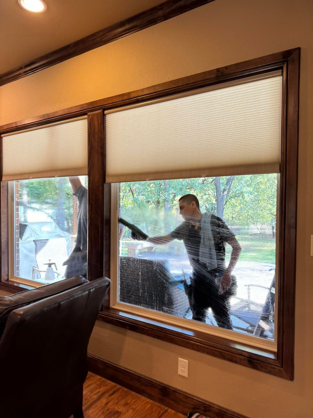 Two men cleaning windows inside a house. One man is actively washing a window with a squeegee.