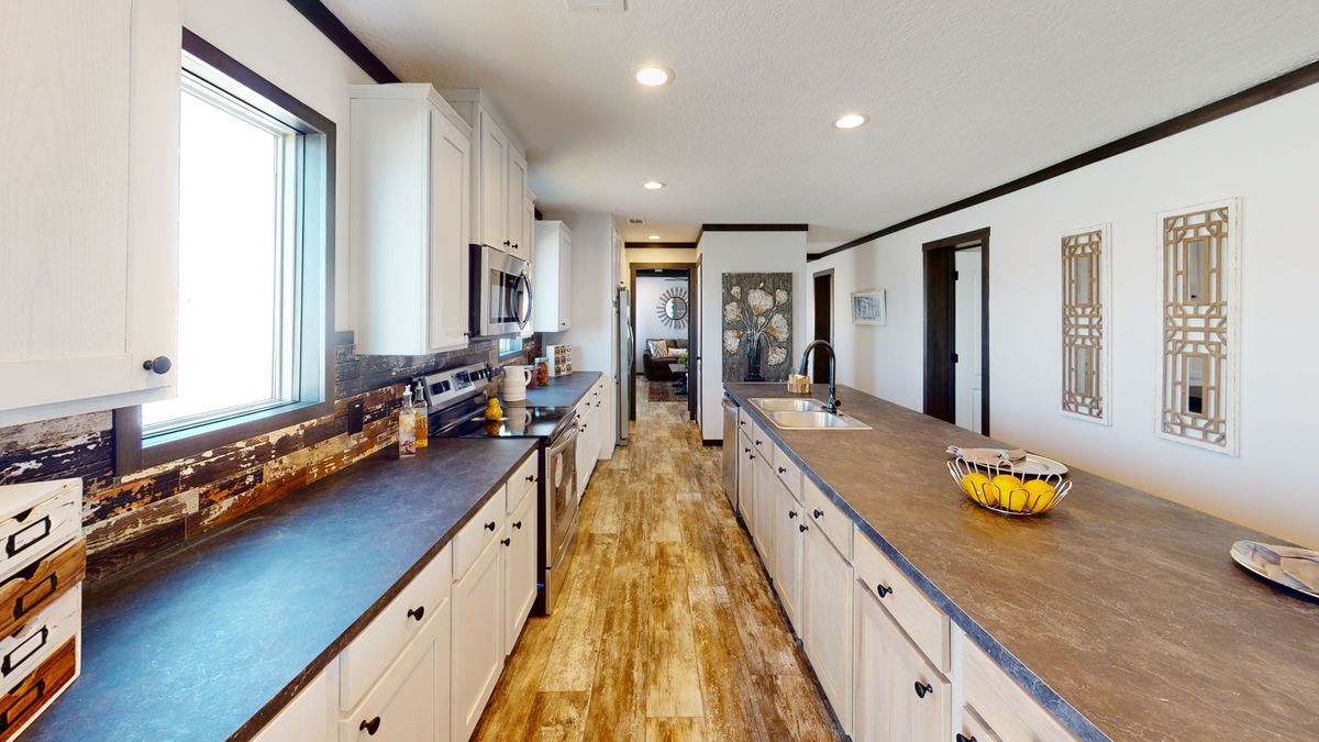 A long kitchen with white cabinets and black counter tops.
