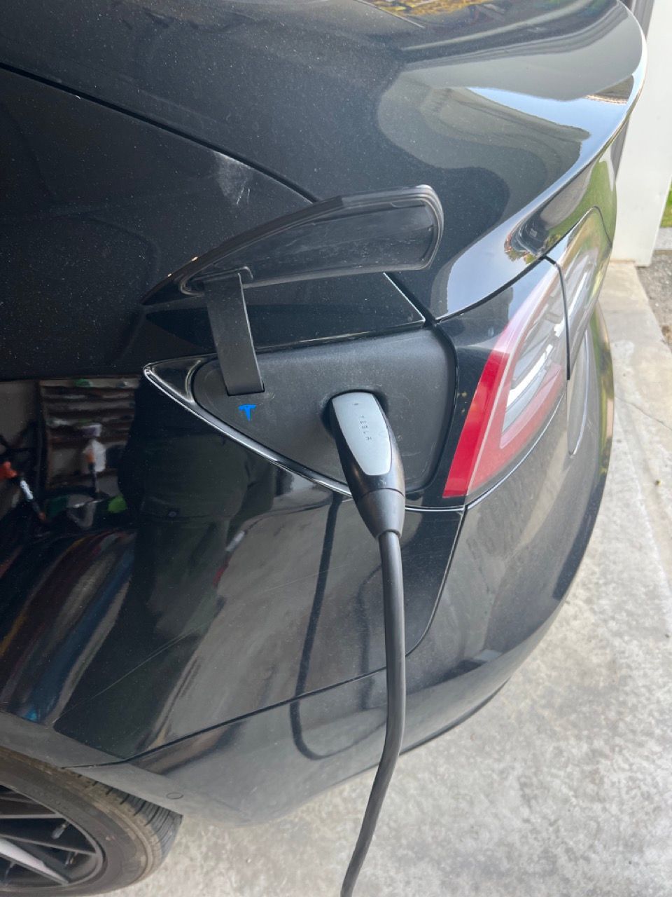 A black tesla model 3 is charging in a garage.