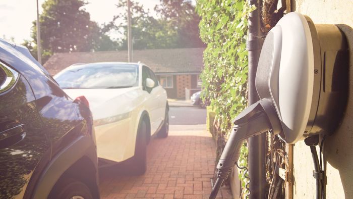 Two cars are parked in a driveway next to a charging station.