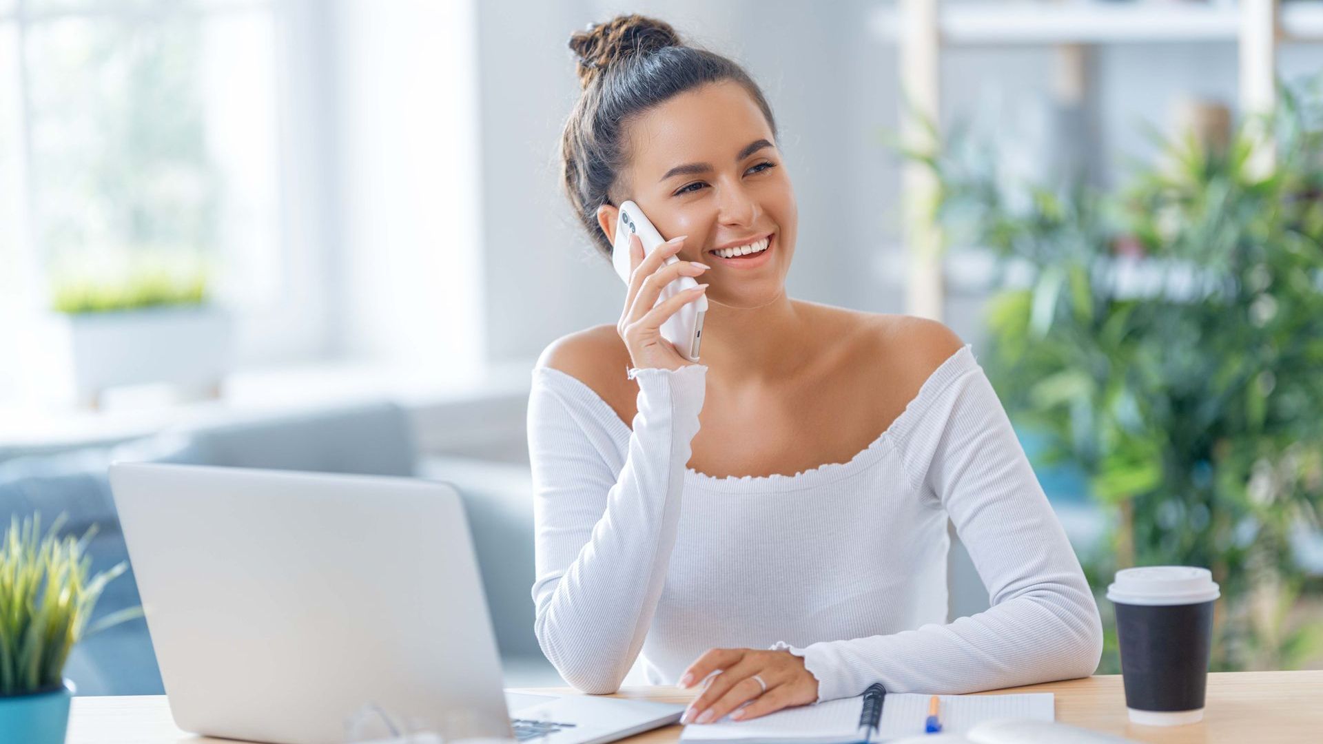 A woman is sitting at a desk talking on a cell phone.